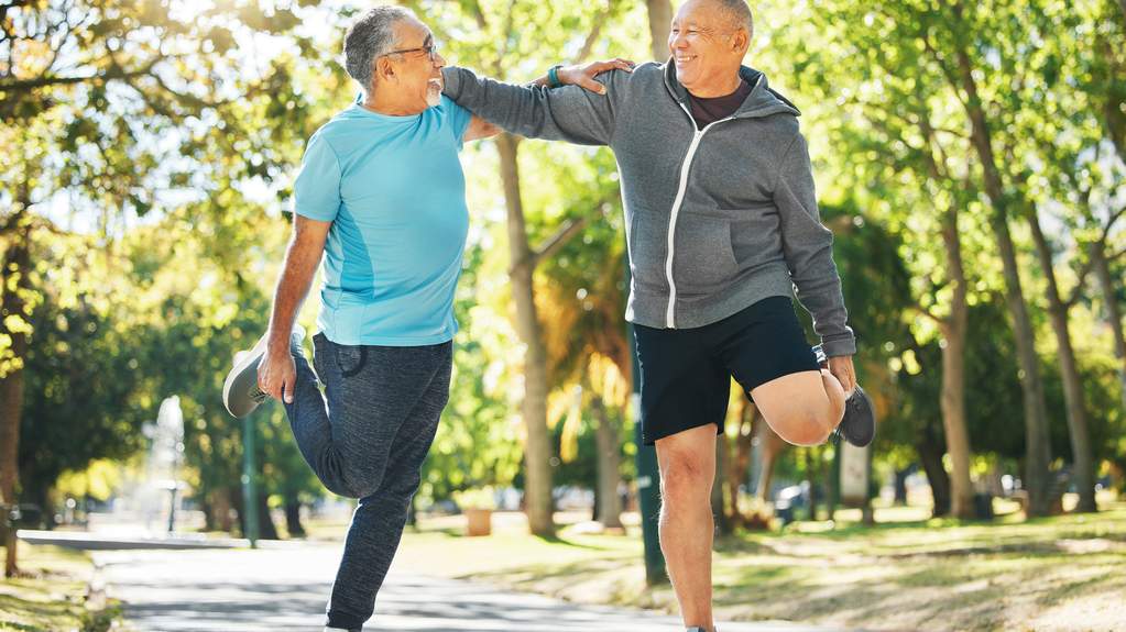 A small group of older adults doing tai chi together outdoors on a calm morning