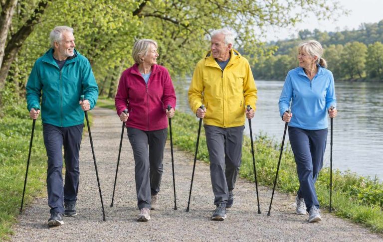 Four older adults Nordic walking with poles along a riverside path in spring