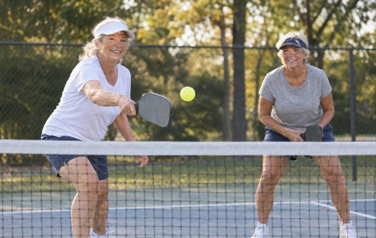 Two older women playing pickleball at the net on an outdoor court