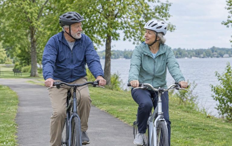 An older couple riding bicycles slowly on a flat park trail